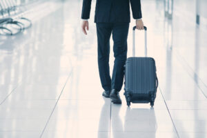 Uomo d'affari in abito elegante che cammina in aeroporto trascinando un trolley rigido nero su pavimento lucido