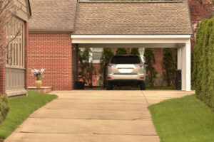 Automobile argentata parcheggiata sotto un portico in un vialetto privato, davanti a una casa in mattoni rossi con giardino curato.