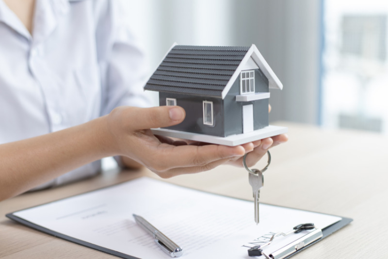 Persona che tiene in mano un modellino di casa e una chiave sopra un contratto assicurativo, simbolo di protezione dell’abitazione e scelta della polizza casa.